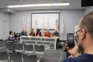 Photo de conférence de presse au CCQCA, 5 personnes à une table, une personne qui filme sur son cellulaire