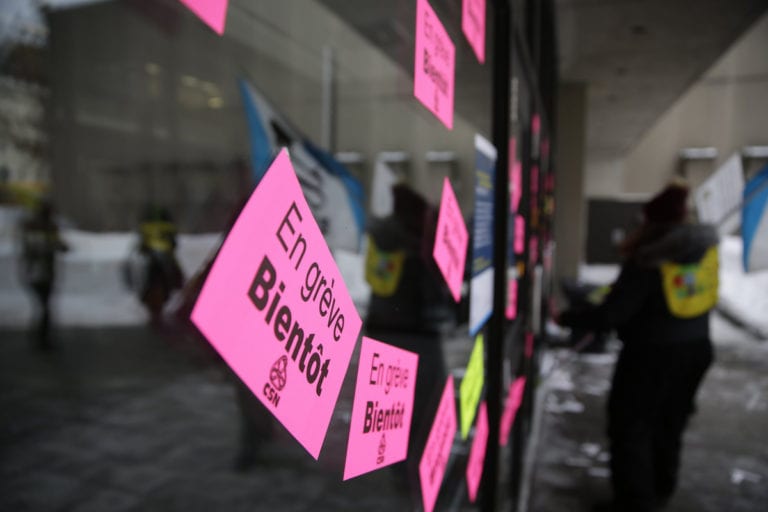 Autocollants sur une vitrine annonçant une grève bientôt dans les RSG. On remarque également une travailleuses avec un dossard RSG et le drapeau de la FSSS-CSN.